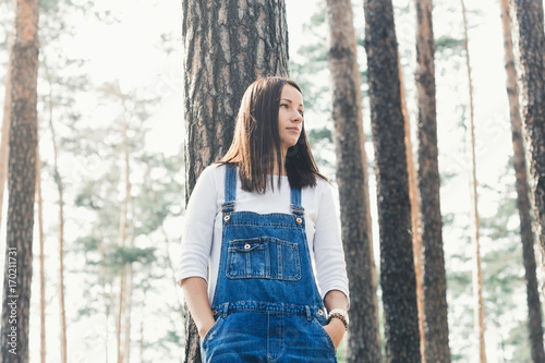 Konstfotografi Beautiful young woman in jeans overalls standing in woodland