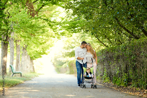 Mother, father and baby in a stroller walk along the alley in the park. © Studio Romantic