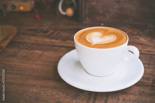 Fotografia Drak tone filter,Close up white coffee cup with heart shape latte art on wood ta