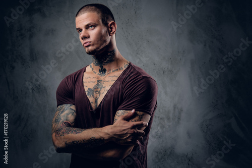 Tattooed male with crossed arms over grey background.