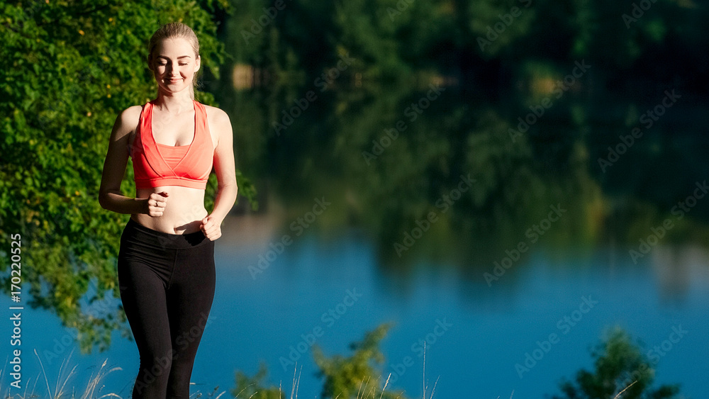 young blond woman running on nature. A sports girl in a red T-shirt runs along the park near the river.