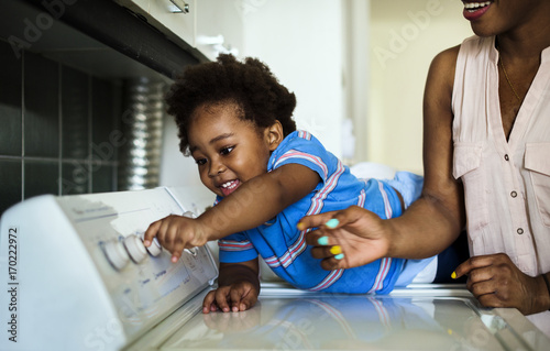 Fotografija African descent kid helping mom doing the laundry