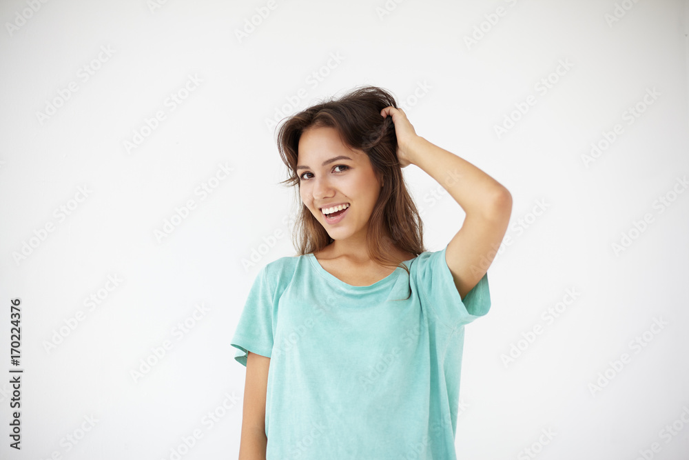 Natural beauty and youth concept. Picture of cheerful playful young Hispanic female with fresh skin and brown eyes touching her long dark hair and grinning broadly at camera, enjoying leisure time Natural beauty and youth concept. Picture of cheerful playful young Hispanic female with fresh skin and brown eyes touching her long dark hair and grinning broadly at camera, enjoying leisure time