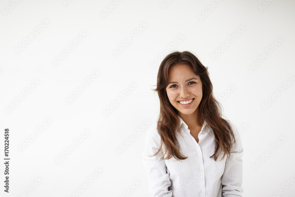 Isolated picture of natural positive young woman employee of mixed race appearance dressed in white blouse, looking at camera with pleased joyful smile, happy after she got promotion at work Isolated picture of natural positive young woman employee of mixed race appearance dressed in white blouse, looking at camera with pleased joyful smile, happy after she got promotion at work