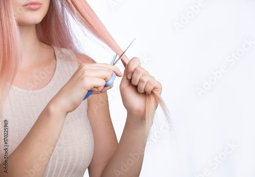 Young girl with golden pink hair cutting her hair with scissors. Isolated on white