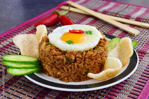 Nasi goreng fried rice with shrimps and egg garnished with fresh cucumber slices and prawn crackers on a plate on a cloth. Asian food