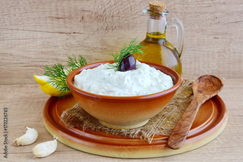 Tzatziki - yoghurt sauce with cucumber, dill, olive oil, lemon and garlic in a traditional bowl,traditional greek cuisine.Twooden background. op view photo