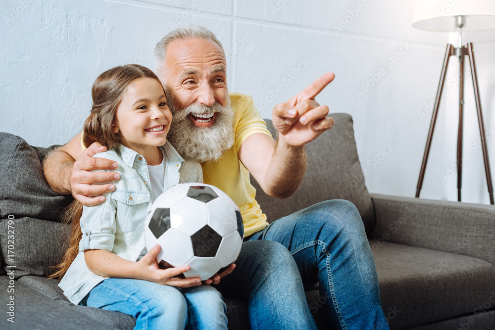 Grandfather and granddaughter laughing at funny moment during football