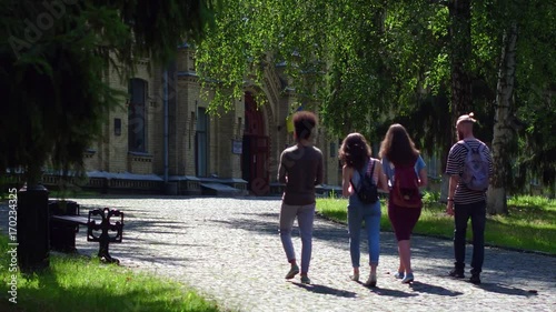 Rear view of students slowly walking in college park. Sunny day, young people going to college.