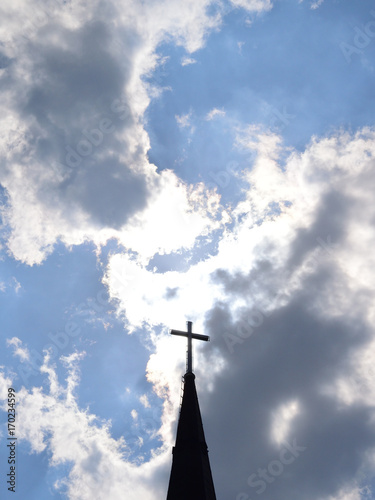The cross over the church spire and the sun obscured by clouds