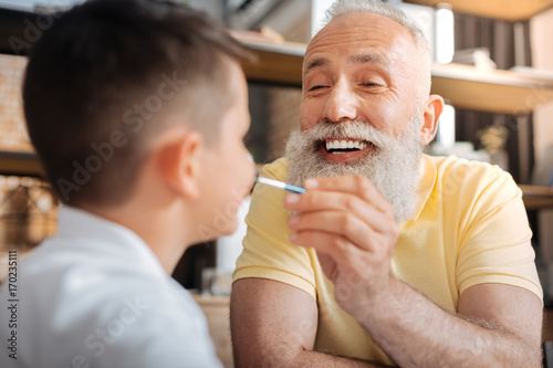 Cheerful senior man putting a paint dot on grandsons nose