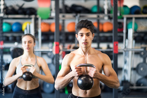 Fototapeta Naklejka Na Ścianę i Meble -  Young fit couple in gym exercising with kettlebell.