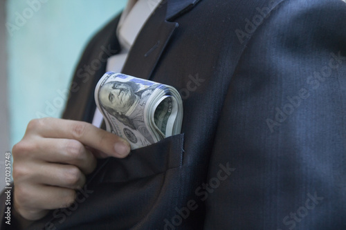 Foto A man in a jacket or a tuxedo puts a bundle of hundred-dollar bills in his breas