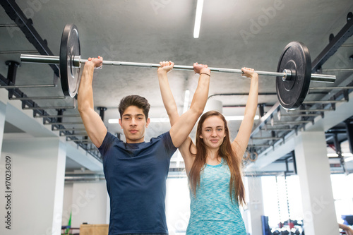 Young fit couple in gym lifting heavy barbell.