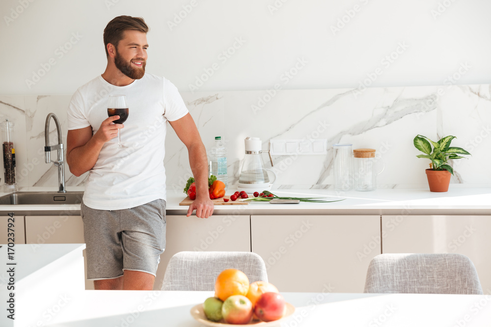 Smiling bearded man standing on kitchen with ice drink Smiling bearded man standing on kitchen with ice drink