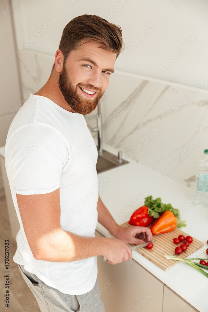 © Drobot Dean - Vertical image of smiling bearded man cuts vegetables on kitchen