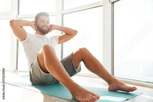 Smiling Handsome bearded man doing abdominals exercises near the window