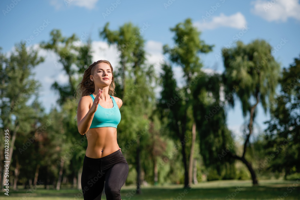 Young happy female runner running in city park. Healthy fitness woman jogging outdoors. Forest in background.