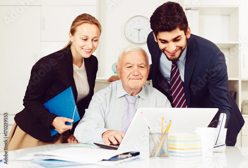 Employees are demonstrating reports on laptop to mature boss