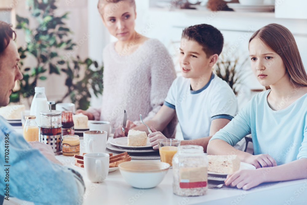 Puzzled teenage girl looking into vacancy during breakfast with family