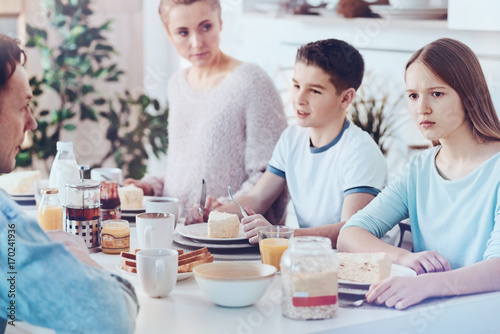 Puzzled teenage girl looking into vacancy during breakfast with family