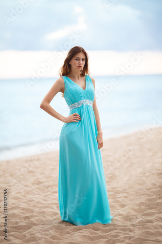Beautiful young girl in a light blue long dress on the beach 