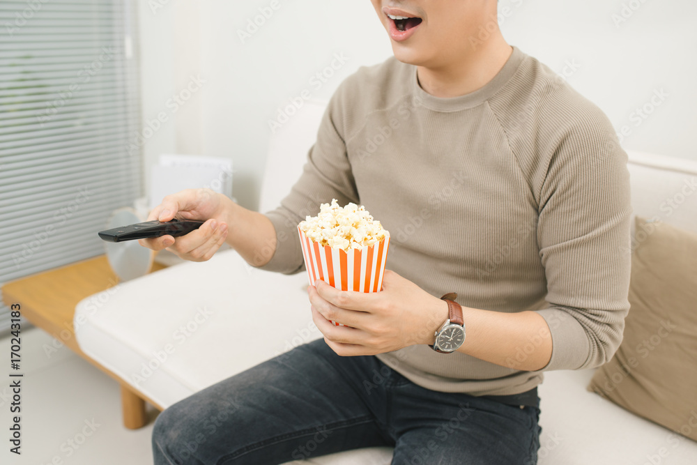 Young man eating popcorn and watching movies relaxed on couch at home