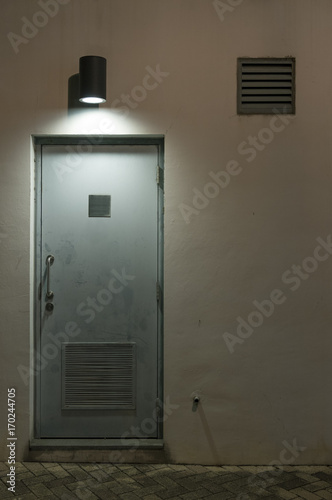 Light, air vent and door on wall at night