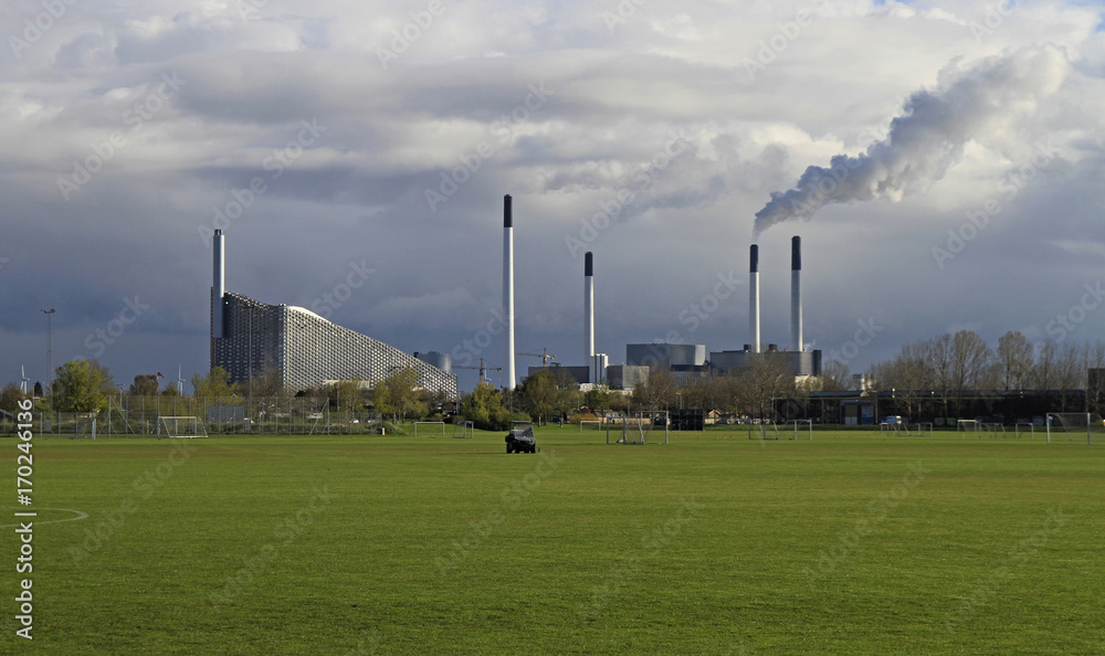 green football field against the background of smoking chimneys