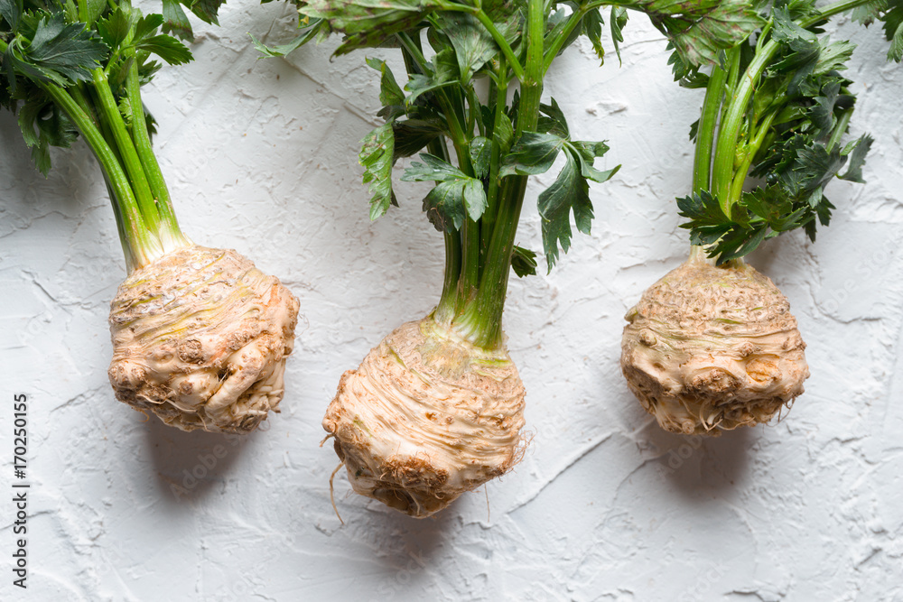 Fotografie Celery roots with green leaves on a white table