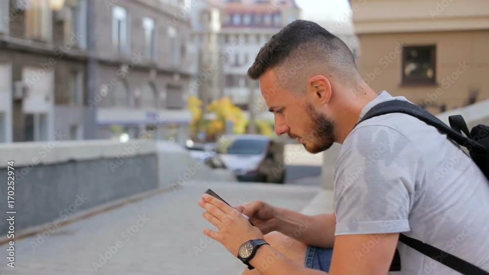 Young guy sits on the steps in the city and plays a game on the phone Young guy sits on the steps in the city and plays a game on the phone