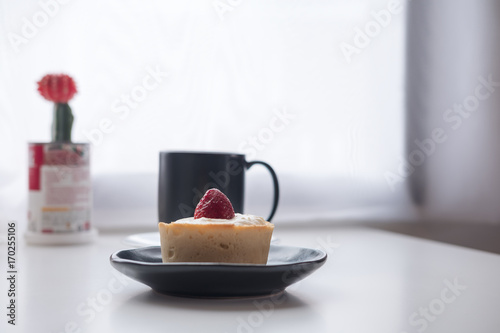 A strawberry cheese tart   a black cup of hot coffee and cactus on white vintage wooden table and curtain background in minimalism cafe