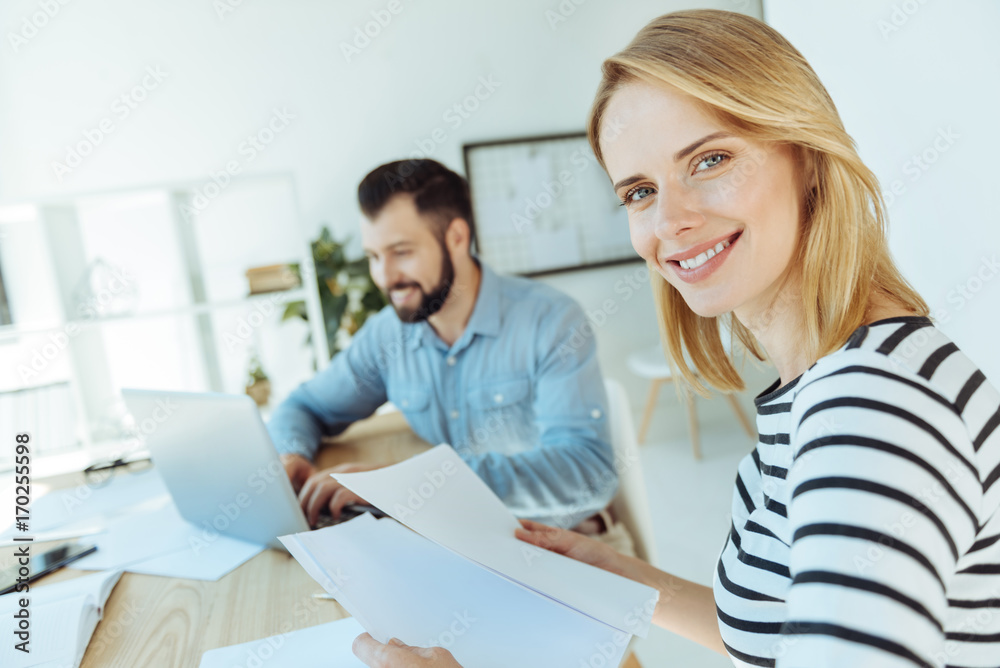 Cheerful woman holding documents and smiling at camera Cheerful woman holding documents and smiling at camera