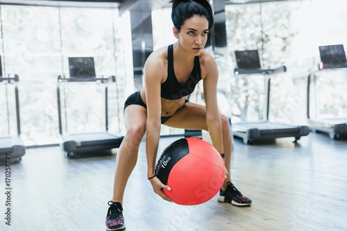 Muscular athletic woman doing squats workout in gym. Strong female squatting  on fitness mat with weight medicine ball in health club. Sport, people and lifestyle concept. © iuricazac