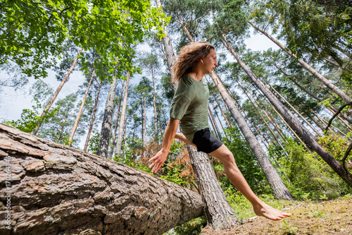 Young man jumping over a tree trunk in the forest.