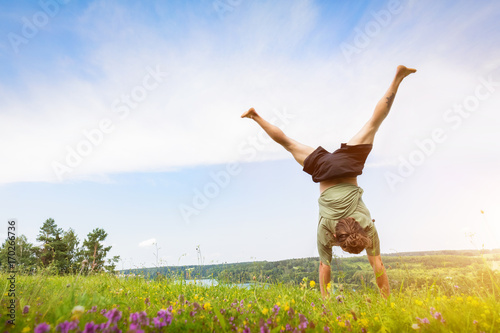 Fotótapéta Young man doing a handstand on a filed.