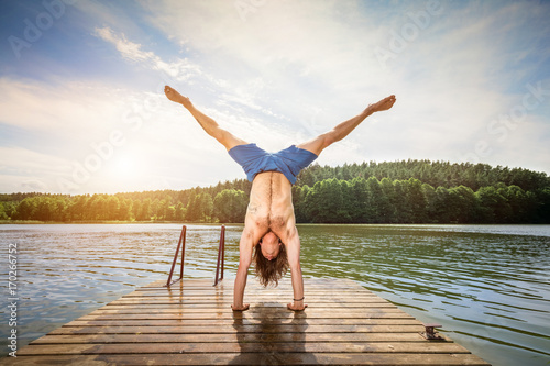 Young man doing a handstand on a wooden jetty