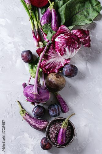 Assortment raw organic of purple vegetables mini eggplants, spring onion, beetroot, radicchio salad, plums, kohlrabi, flower salt over gray concrete background. Top view with space