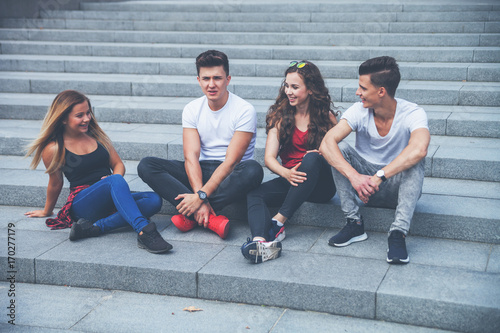 Group of friends sitting together on stairs and talking, city background