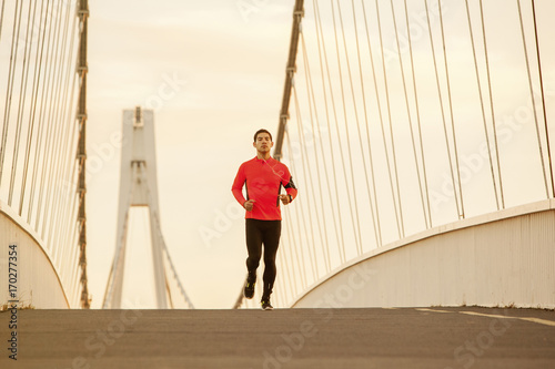 Male runner with headphones jogging over bridge