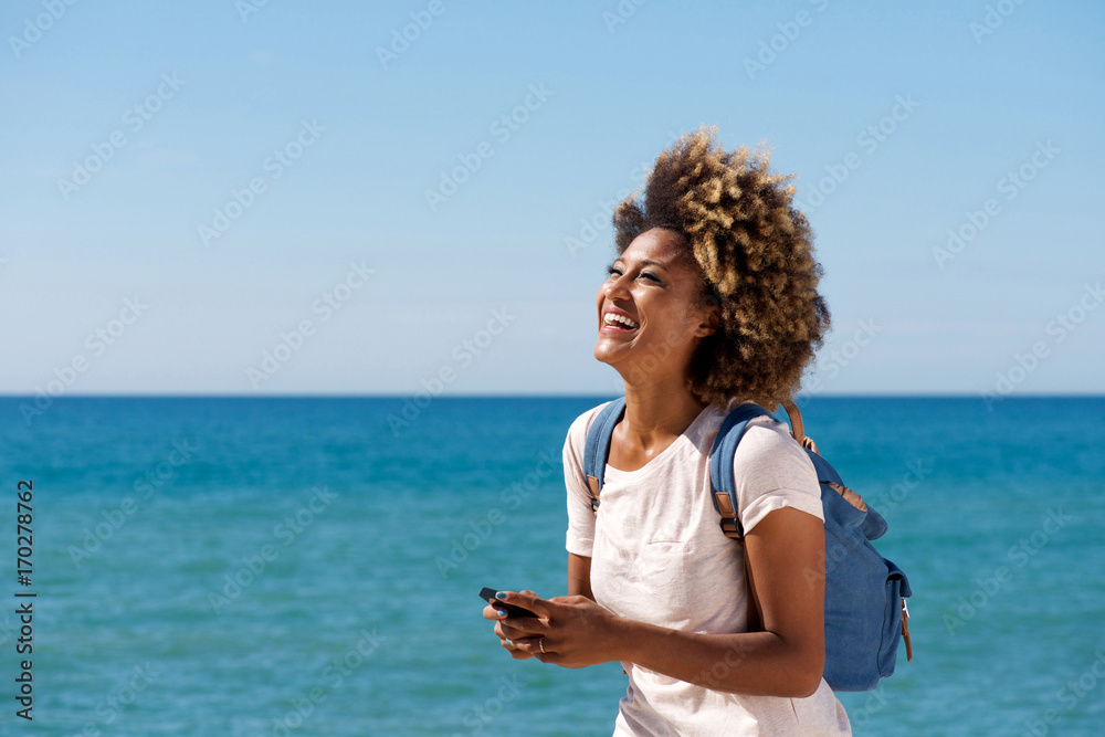 laughing young african woman on the beach with mobile phone
