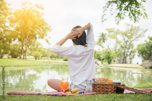 Closeup of young woman streching and relaxing with fruit basket and glass of orange juice in the park at weekend. Wellness. Health and food concept. photo