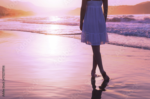 A girl is walking along Crete island coastline at the sunset time, lilac toning.