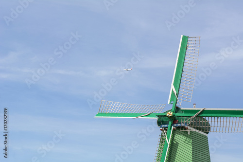 Beautiful green mill under the blue sky with airplane in the summer in Zaanse Schans (Netherlands)