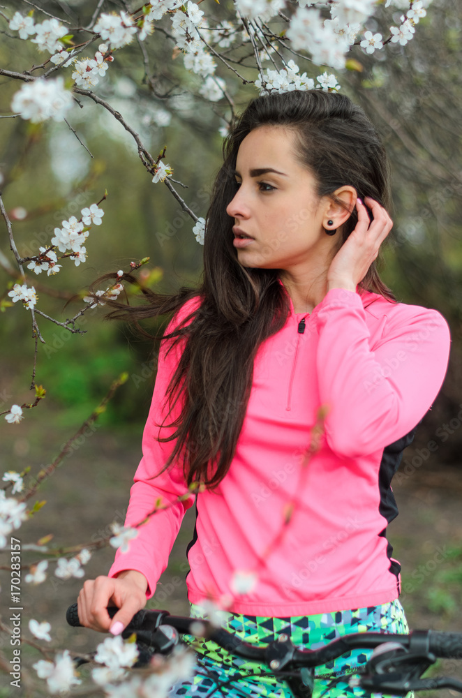 Girl beautiful brunette. Athletic body , pumped muscles. Bright colors , green ,pink . Spring , trees in bloom. She does exercises