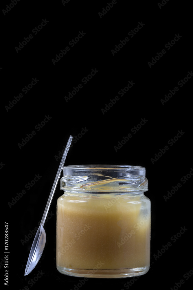 raw organic royal jelly in a small bottle with litte spoon on black raw organic royal jelly in a small bottle with litte spoon on black