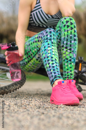 brunette girl in sportswear, riding a Bicycle in the morning in the Park. Resting and drinking water .Closeup of the foot
