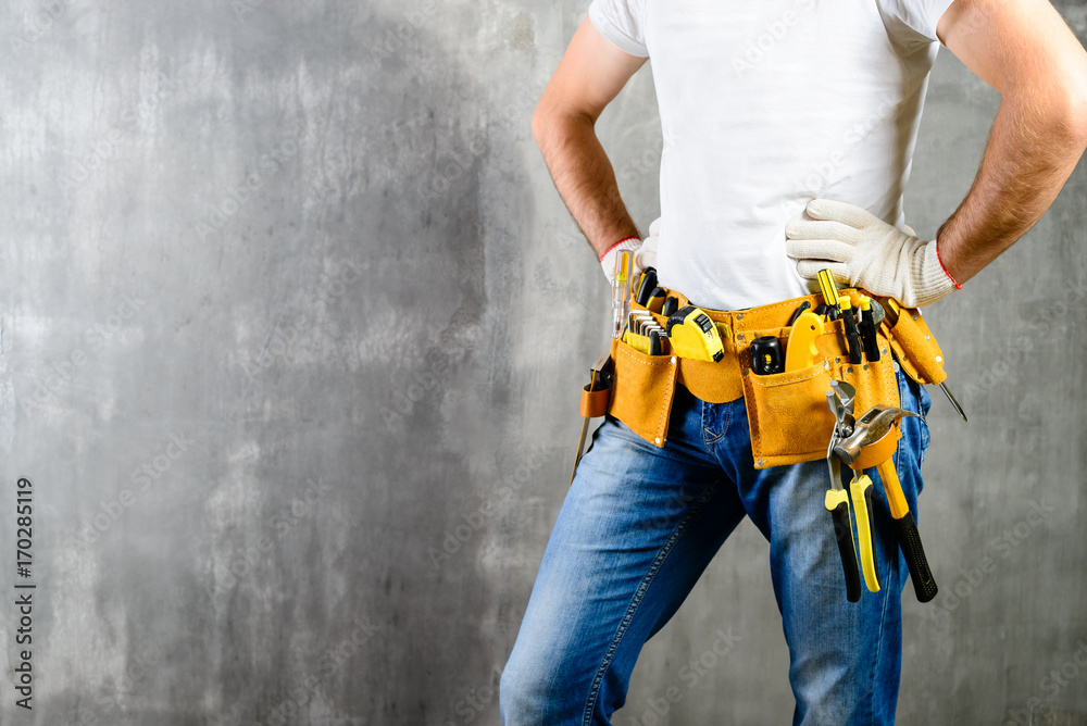 unknown handyman with hands on waist and tool belt with construction tools against grey background with copyspace for text. DIY tools and manual work concept unknown handyman with hands on waist and tool belt with construction tools against grey background with copyspace for text. DIY tools and manual work concept
