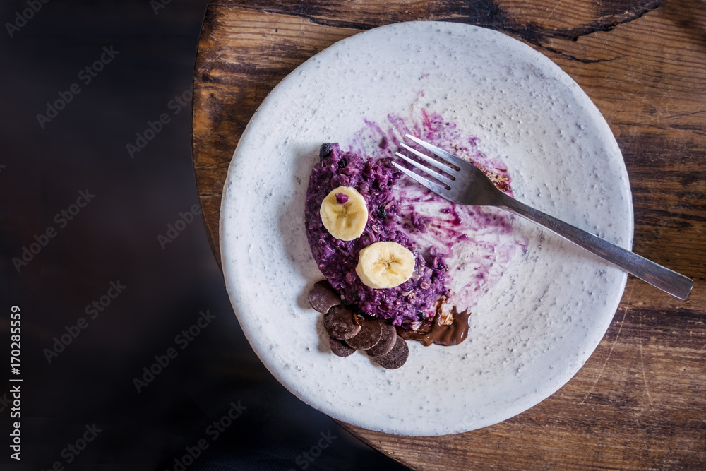 Fototapeta premium White empty plate with blueberry oatmeal dessert leftovers from above on wooden table. Dark food photography
