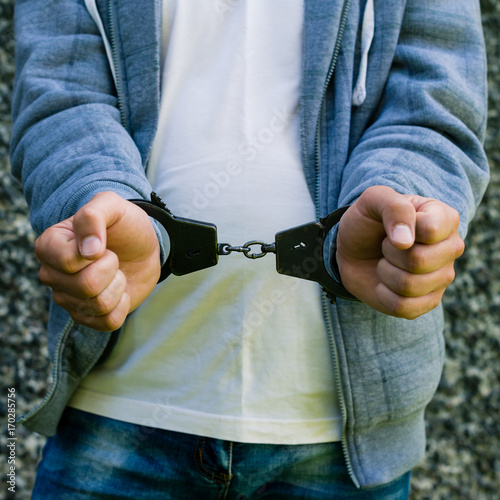 young criminal standing in handcuffs, outdoors. Concept of crime and detention photo